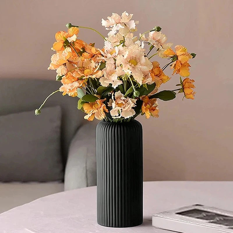 Tall black striped plastic vase with orange and cream faux flower arrangement on round table