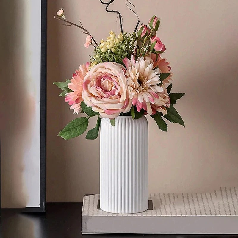 White striped ceramic-look vase styled with soft pink artificial flowers on a modern tabletop