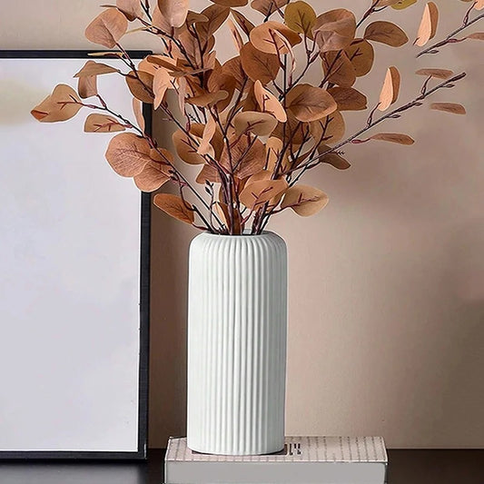 White ceramic-style striped vase decorated with brown faux eucalyptus leaves on a book